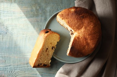 Delicious cut Panettone cake with raisins on light blue wooden table, flat lay. Traditional Italian pastry