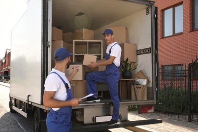 Photo of Moving service workers outdoors, unloading boxes and checking list