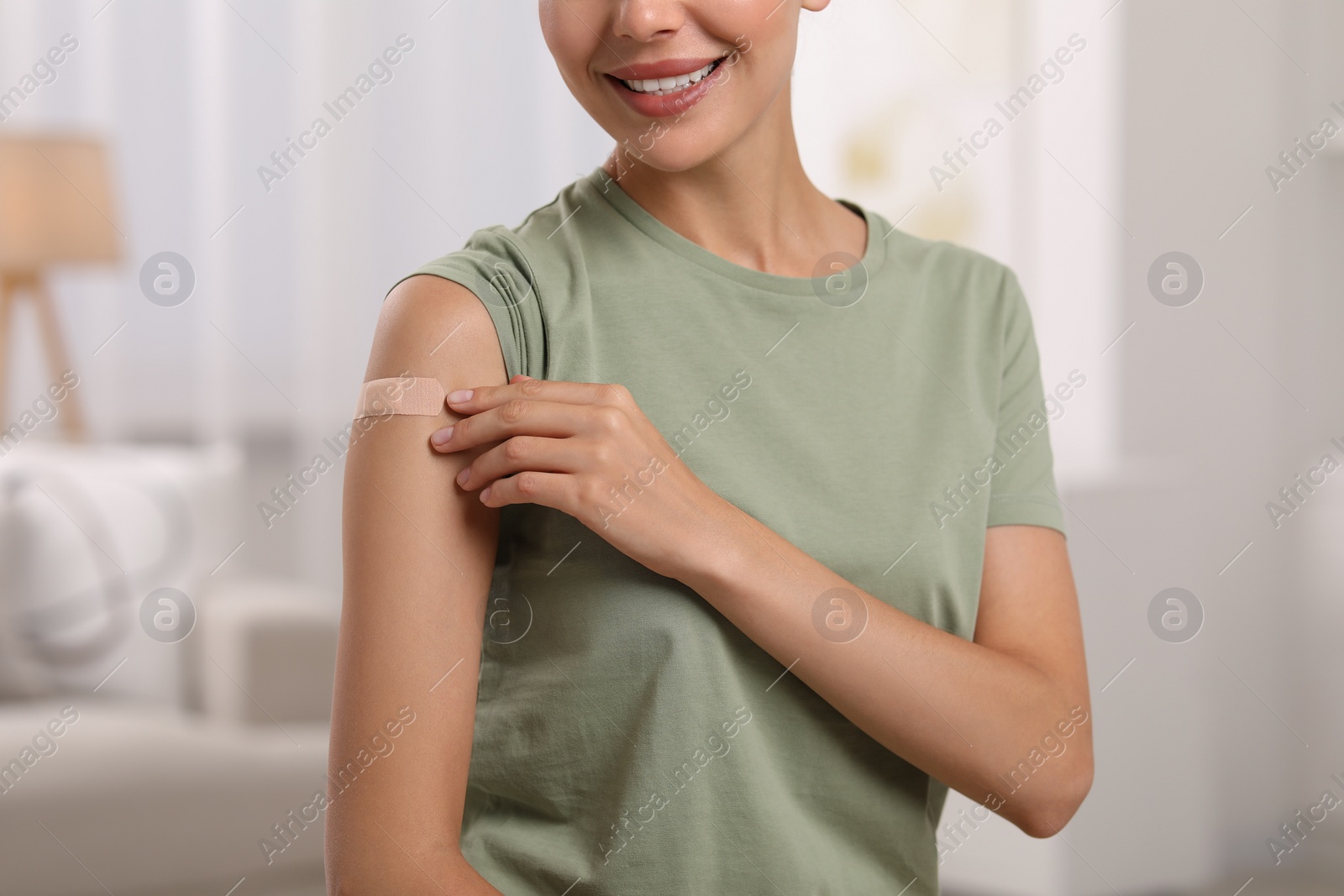 Photo of Woman with sticking plaster on arm after vaccination at home, closeup