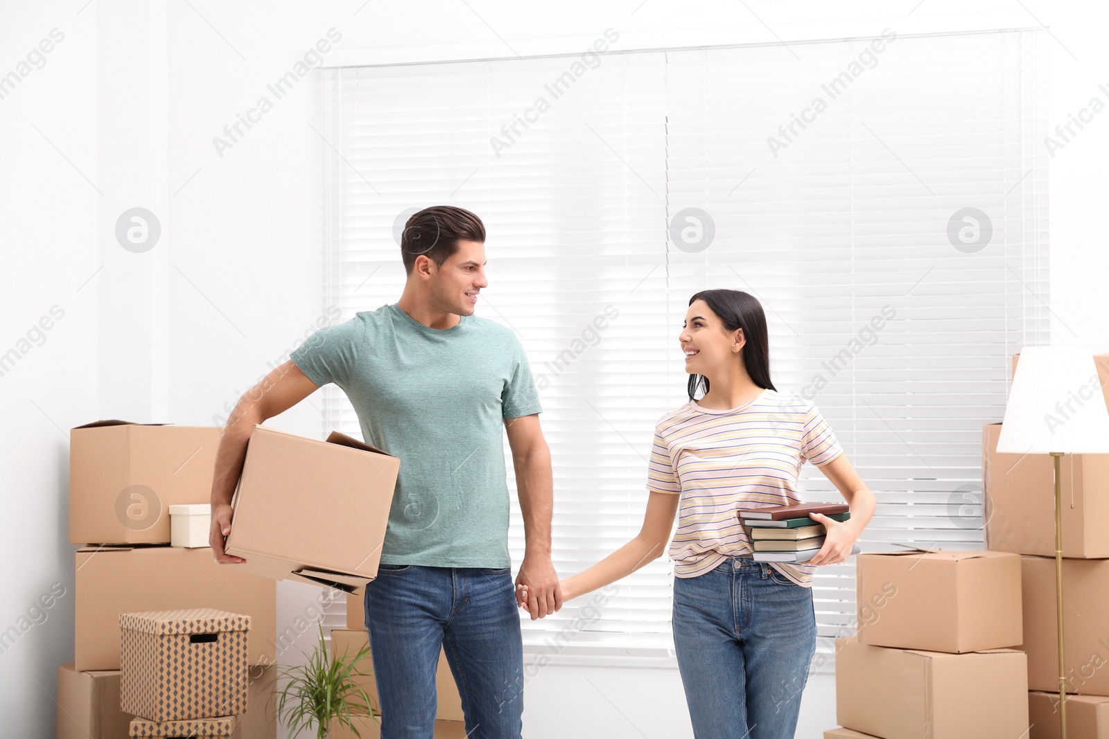 Photo of Happy couple in room with cardboard boxes on moving day