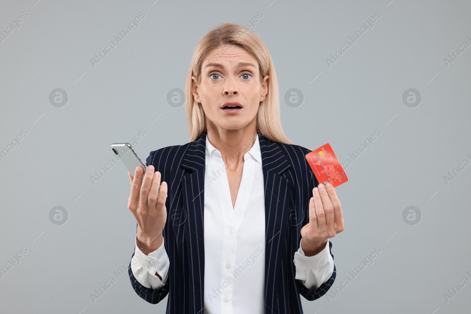 Photo of Stressed woman with credit card and smartphone on grey background. Be careful - fraud