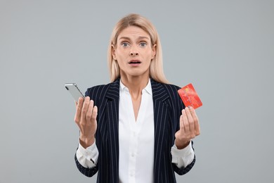 Stressed woman with credit card and smartphone on grey background. Be careful - fraud