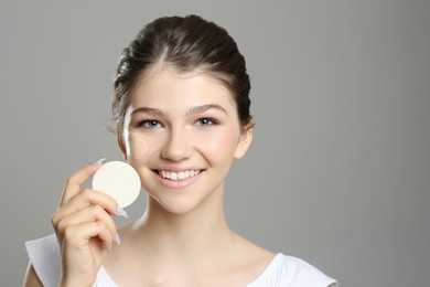 Photo of Beautiful girl with foundation smear on her face holding sponge against grey background
