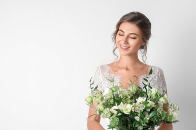 Photo of Young bride wearing wedding dress with beautiful bouquet on light background. Space for text