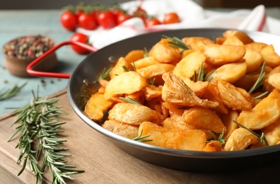 Photo of Dish with baked potatoes and rosemary in wok on wooden board, closeup