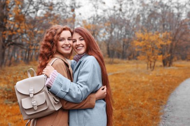 Photo of Portrait of beautiful young redhead sisters in park on autumn day. Space for text