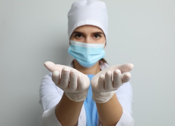 Doctor in protective mask and medical gloves against light grey background, focus on hands