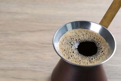 Turkish coffee pot with hot drink on wooden table, closeup. Space for text