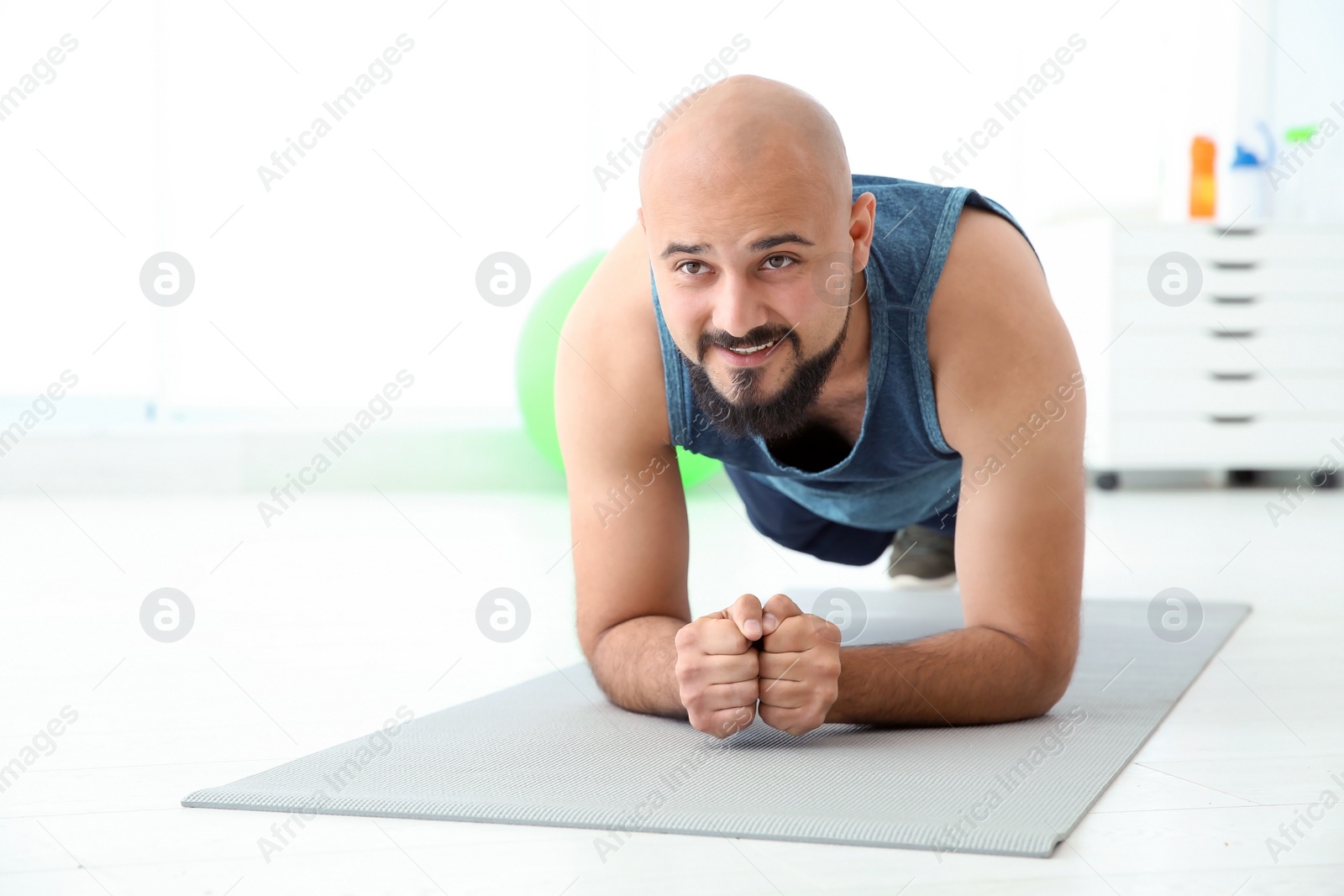 Photo of Overweight man doing plank exercise on mat in gym