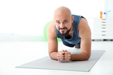 Overweight man doing plank exercise on mat in gym