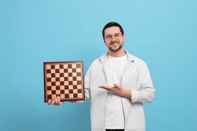 Photo of Handsome man showing chessboard on light blue background