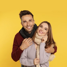 Photo of Happy young couple in warm clothes on yellow background. Winter season