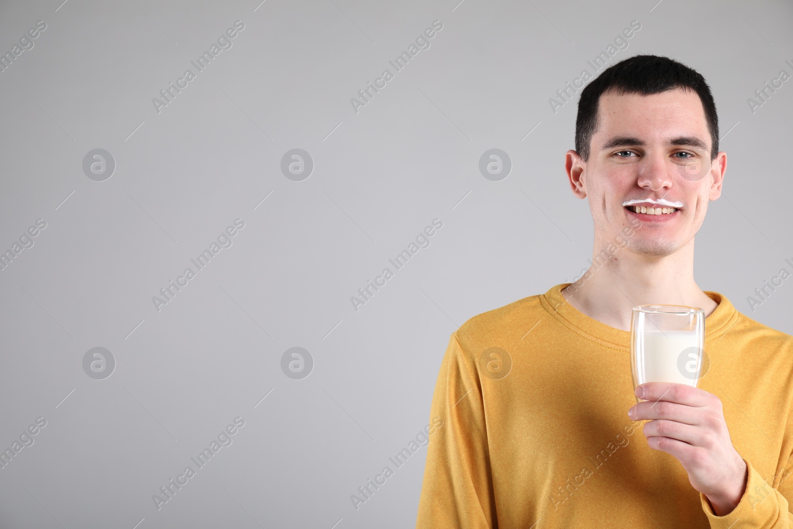 Photo of Happy man with milk mustache holding glass of tasty dairy drink on gray background, space for text