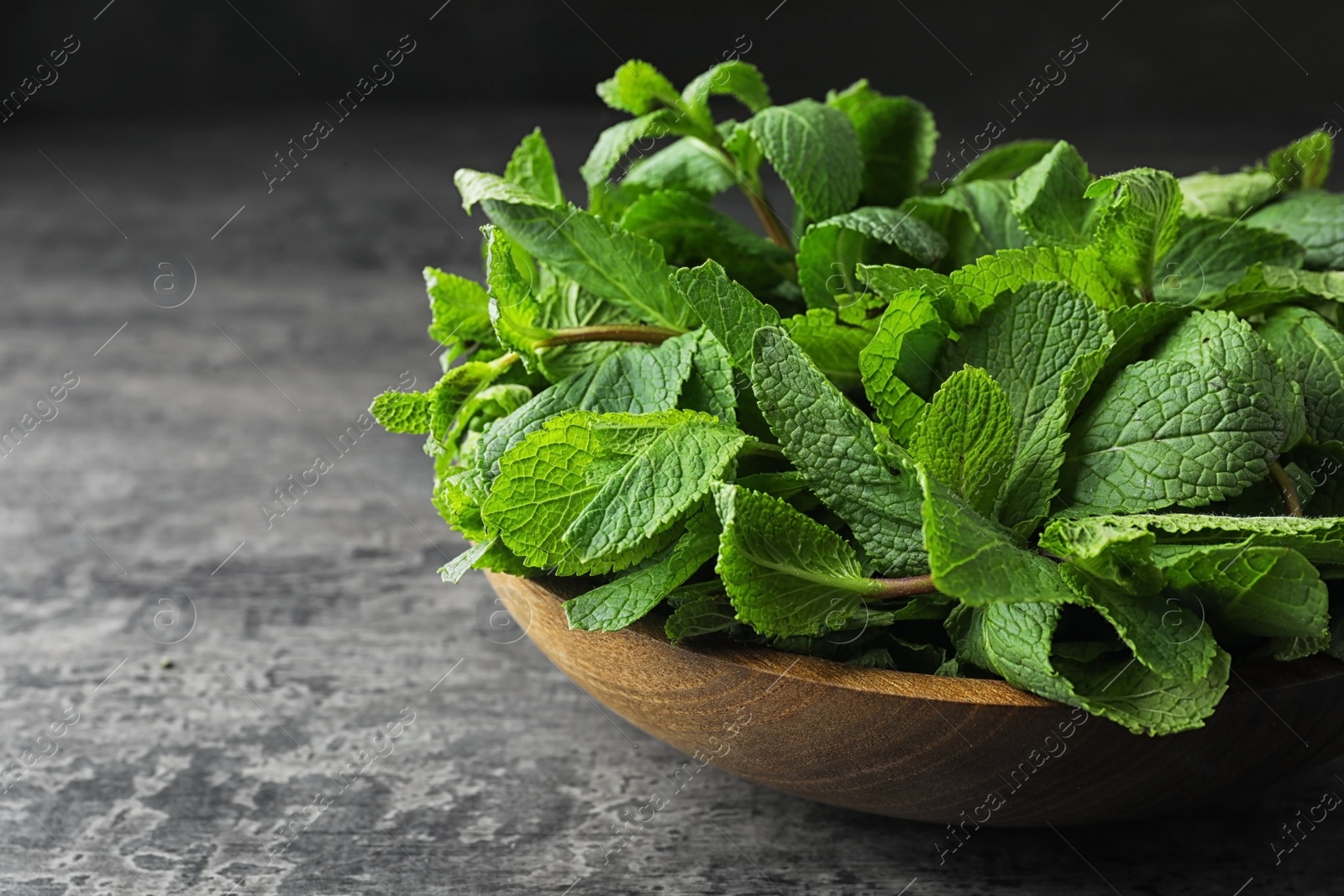 Photo of Wooden bowl full of fresh green mint on grey table, closeup. Space for text