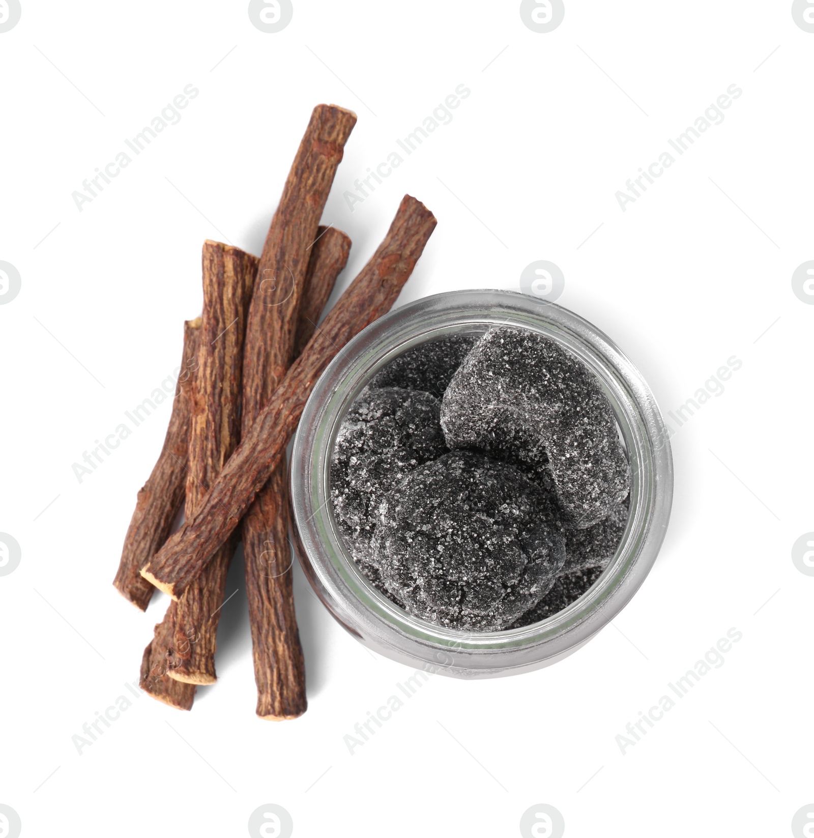 Photo of Glass jar of tasty candies and dried cut liquorice root isolated on white, top view