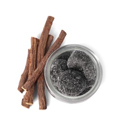 Photo of Glass jar of tasty candies and dried cut liquorice root isolated on white, top view