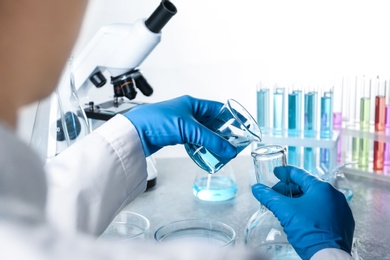 Scientist pouring color liquid from beaker into Florence flask over table, closeup. Solution chemistry