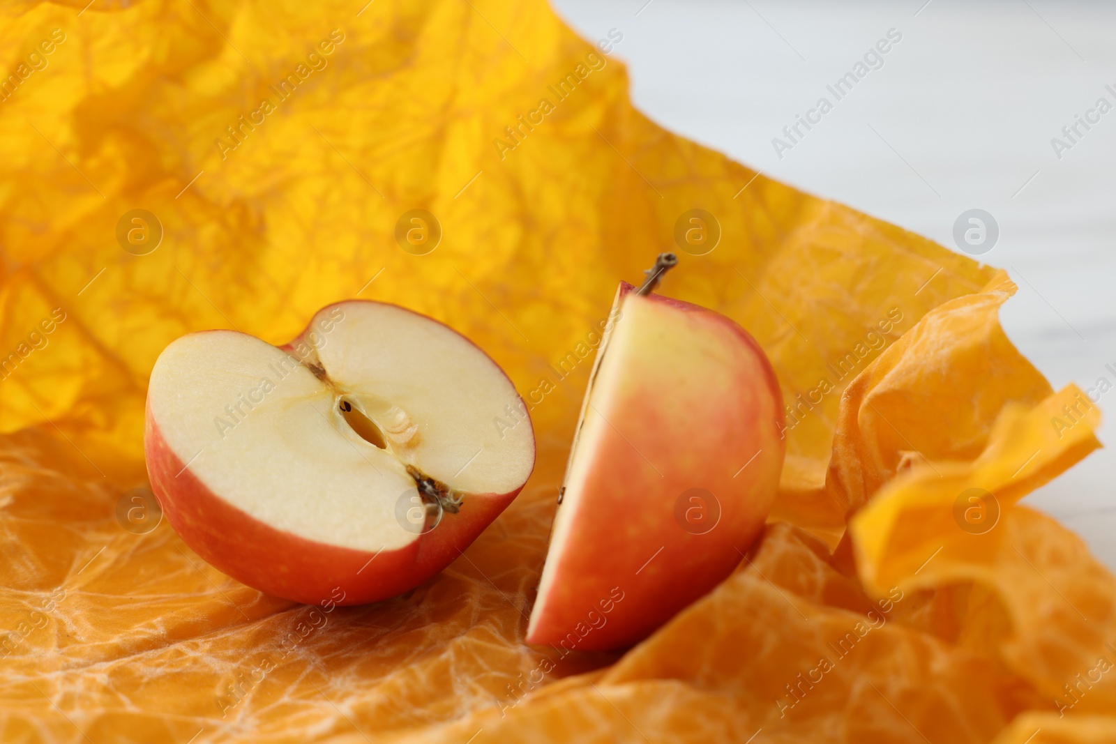 Photo of Halves of apple with orange beeswax food wrap on table, closeup