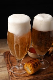 Photo of Glasses with beer and grilled corn on wooden table against black background