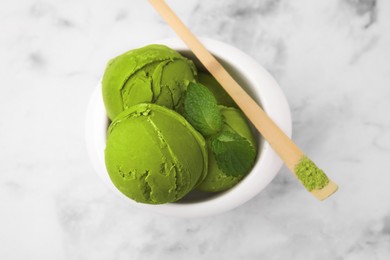 Photo of Tasty matcha ice cream in bowl and spoon with powder on white marble table, top view