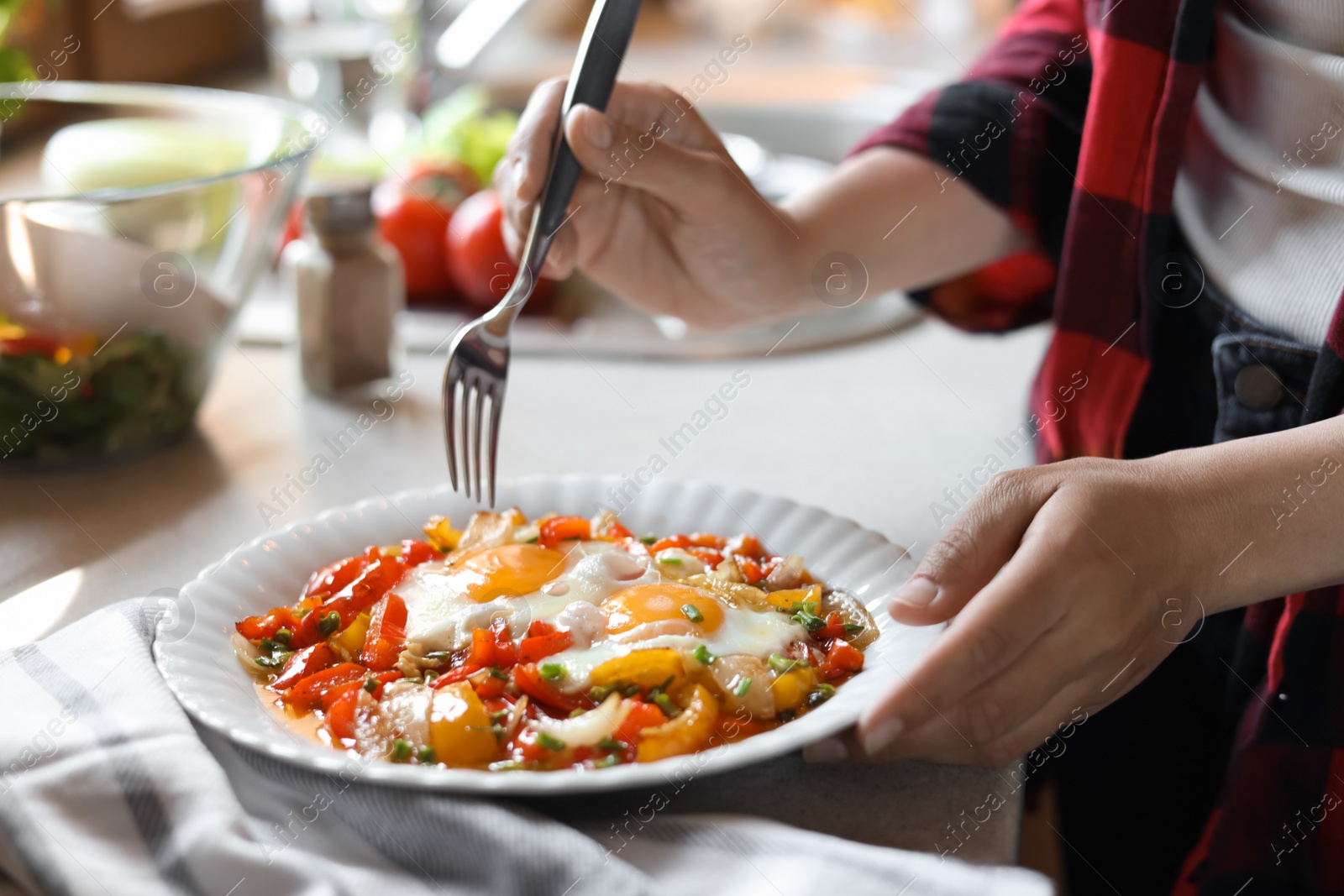 Photo of Woman eating tasty fried eggs with vegetables at table indoors, closeup