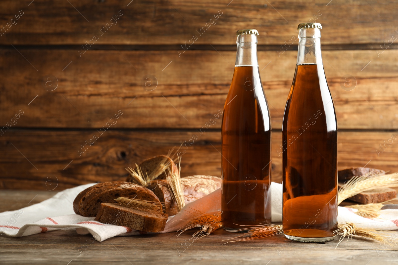 Photo of Bottles of delicious fresh kvass, spikelets and bread on wooden table