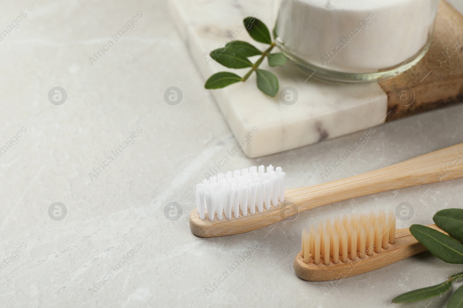 Photo of Bamboo toothbrushes and jar of baking soda on light grey marble table, space for text