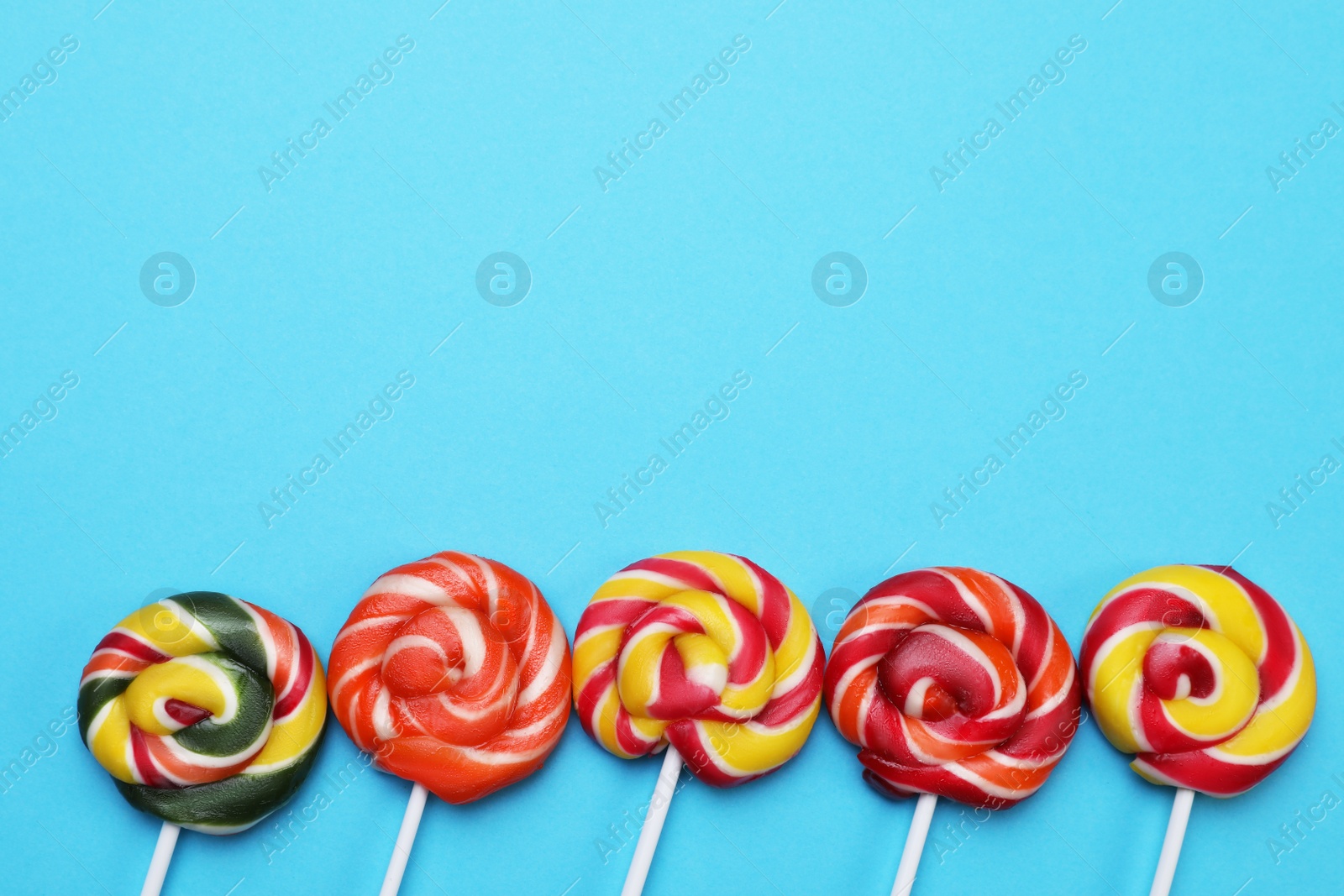 Photo of Sweet lollipops on light blue background, flat lay. Space for text