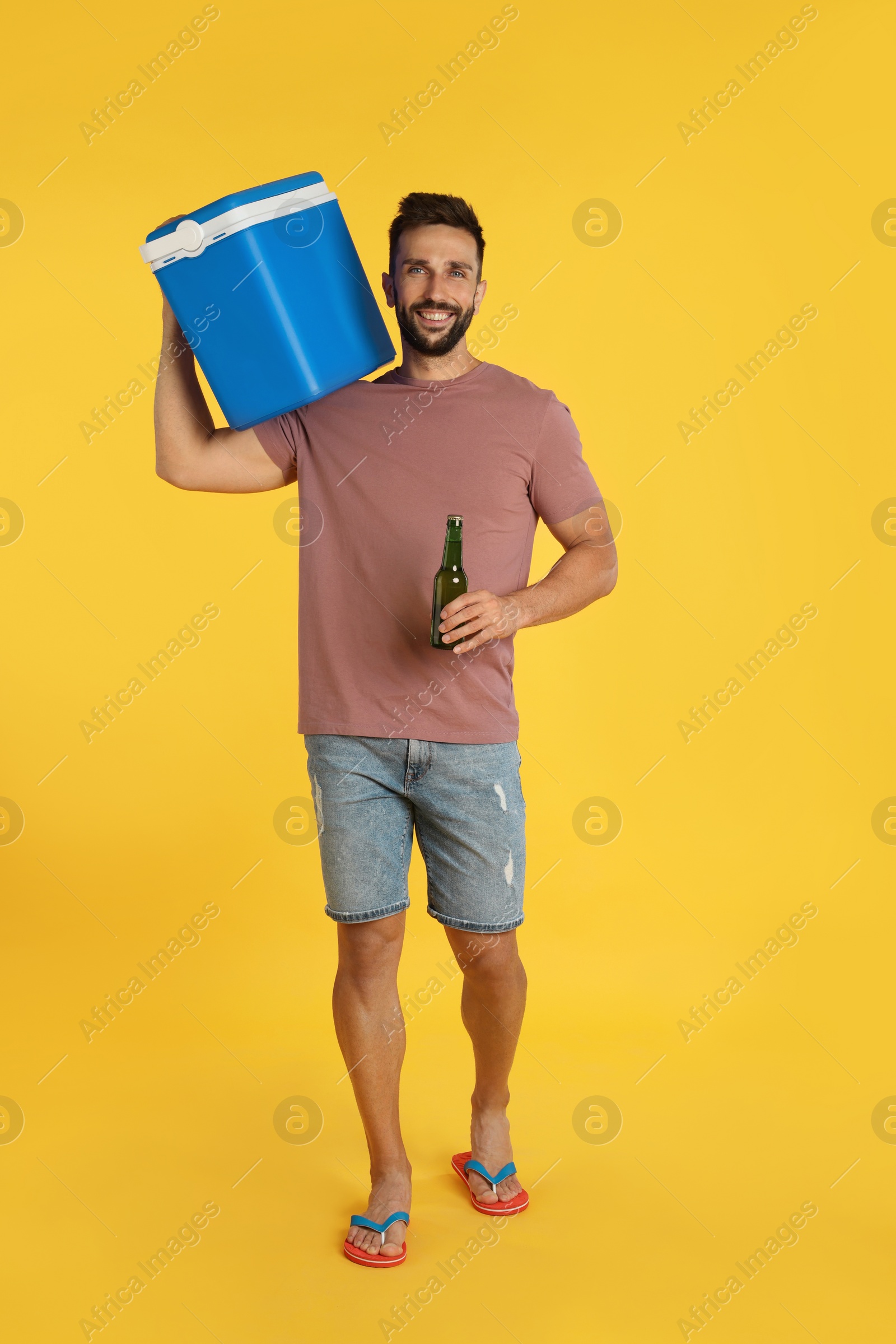 Photo of Happy man with cool box and bottle of beer on yellow background