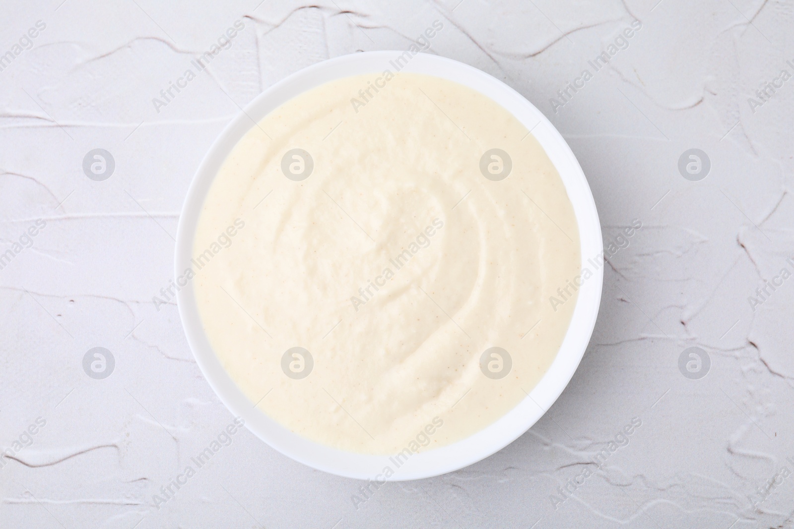 Photo of Delicious semolina pudding in bowl on white textured table, top view