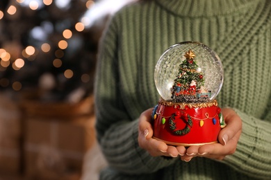 Photo of Woman in warm sweater holding snow globe indoors, closeup