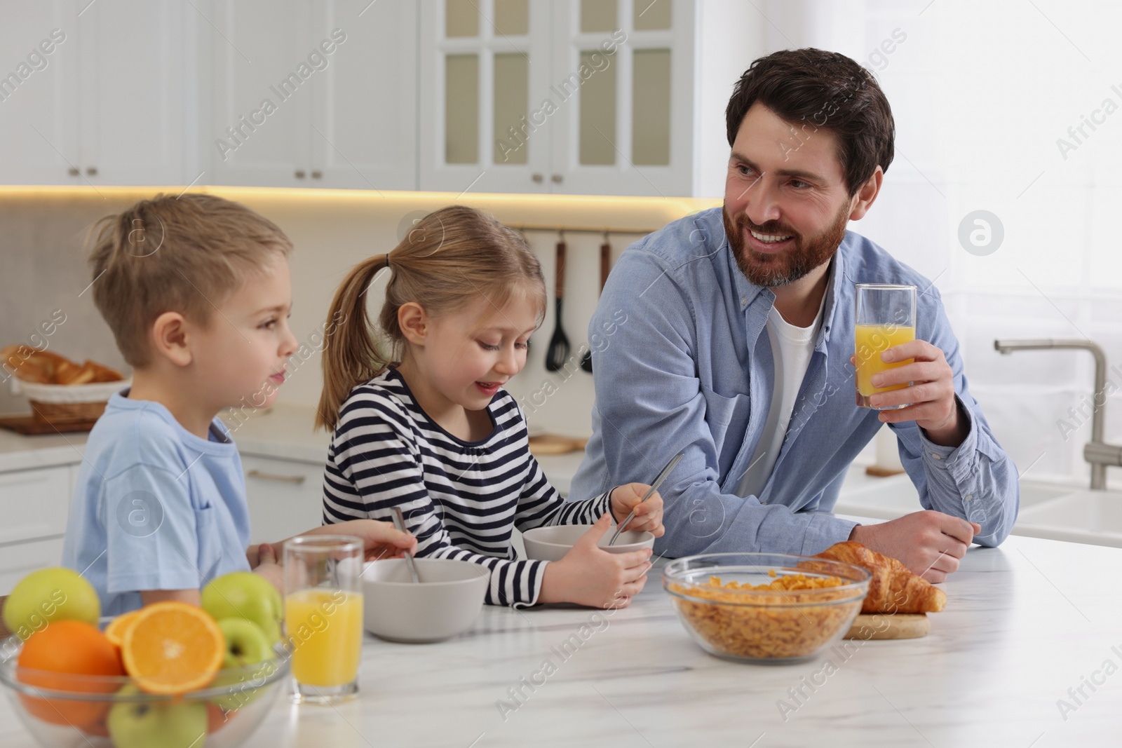 Photo of Father and his little children having breakfast at table in kitchen