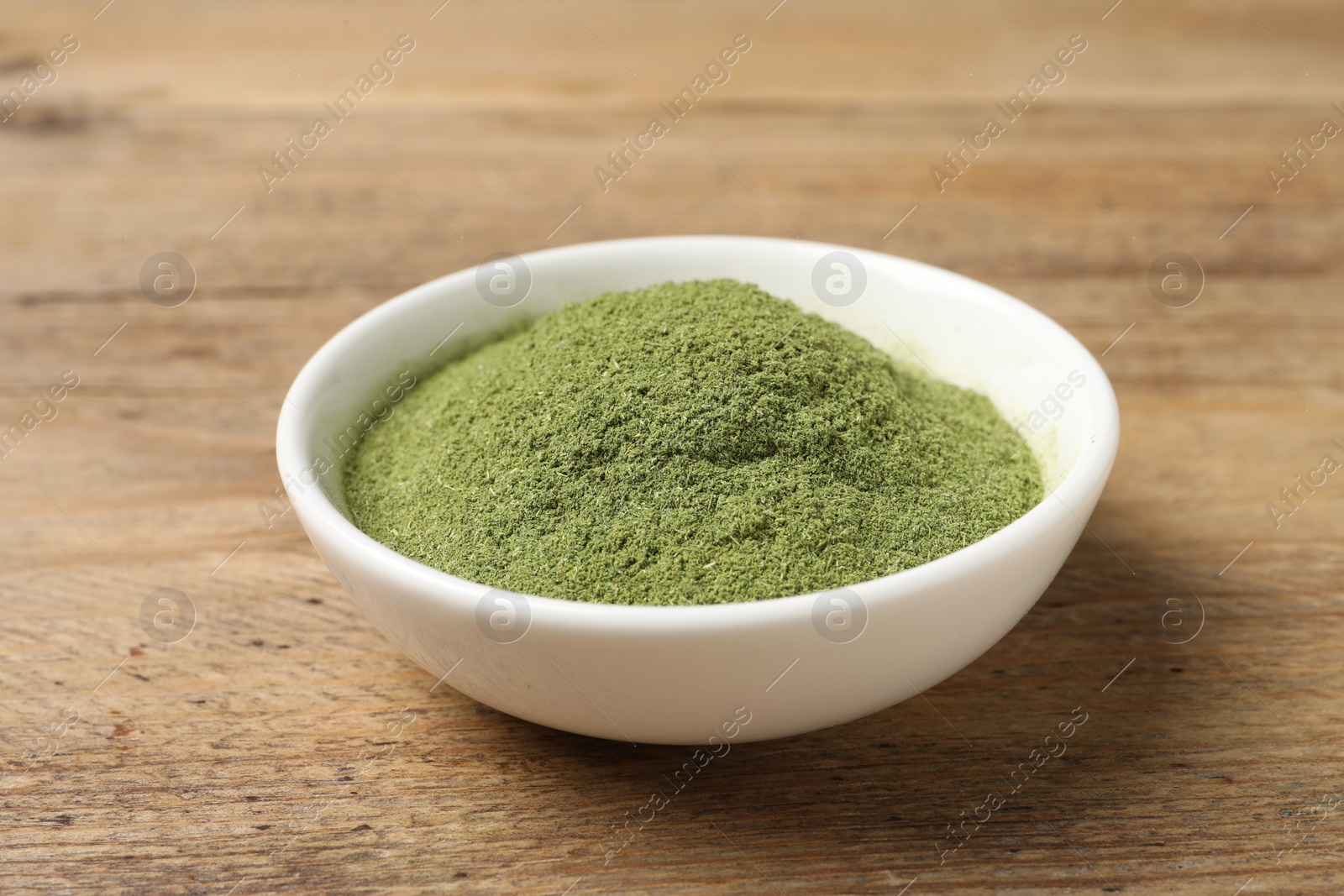 Photo of Wheat grass powder in bowl on wooden table, closeup