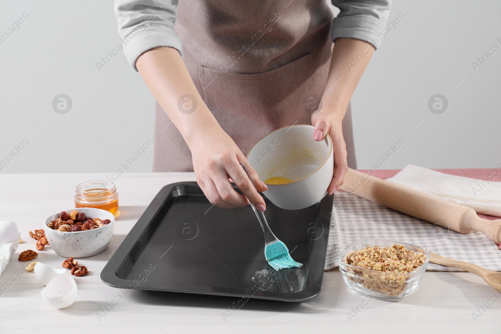 Photo of Making delicious baklava. Woman buttering baking pan at white wooden table, closeup