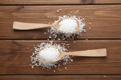 Natural sea salt and spoons on wooden table, flat lay