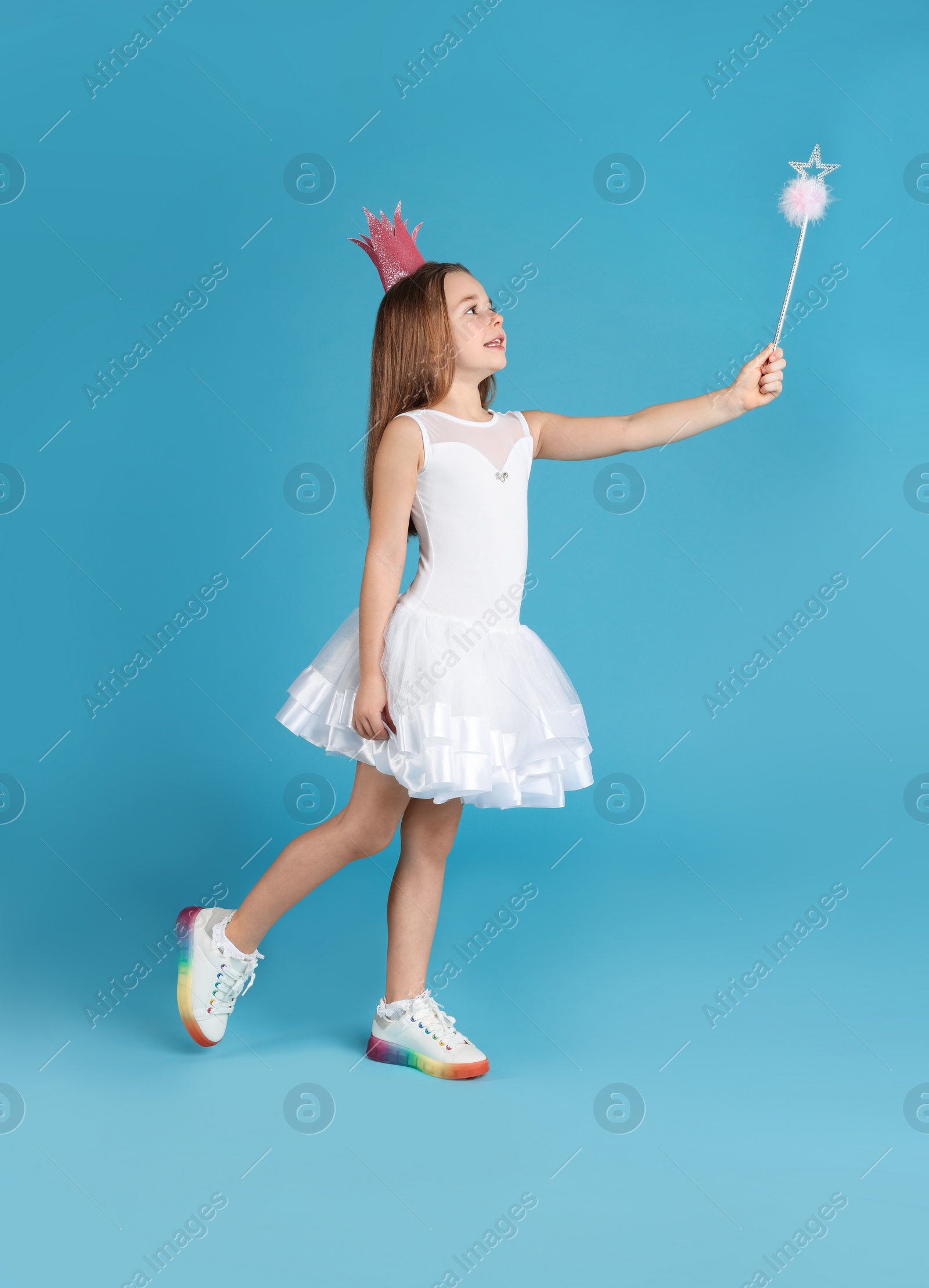 Photo of Cute girl in pink crown with magic wand on light blue background. Little princess