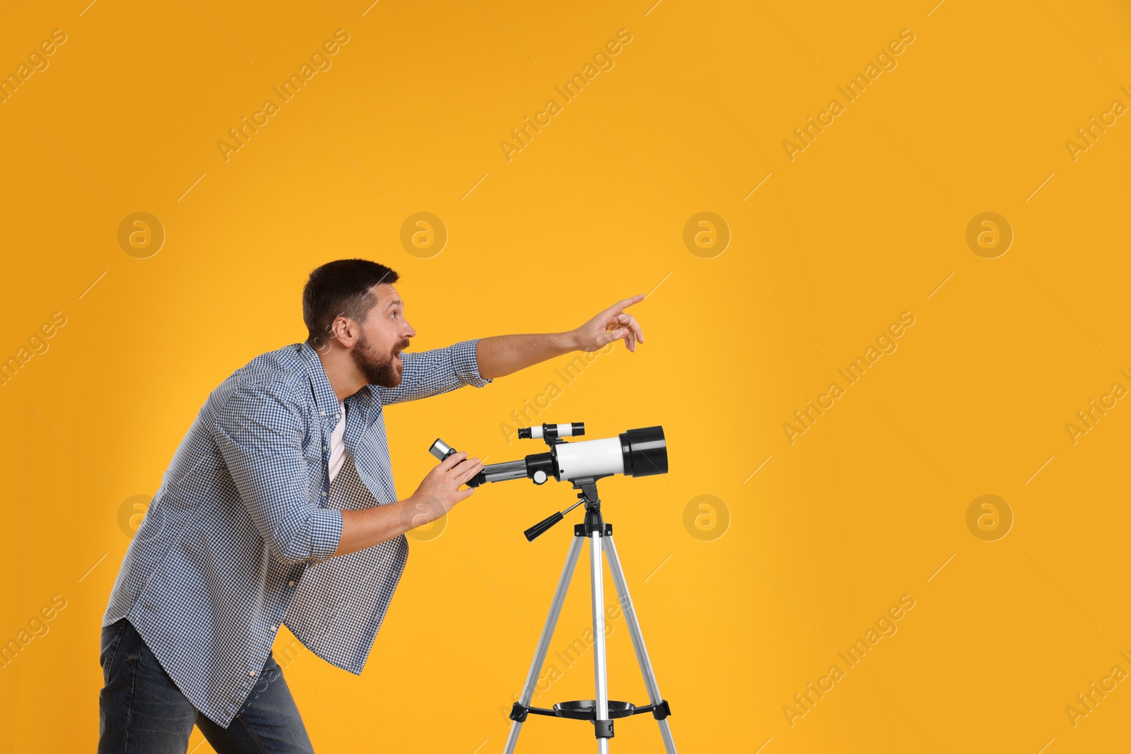 Photo of Excited astronomer with telescope pointing at something on orange background. Space for text