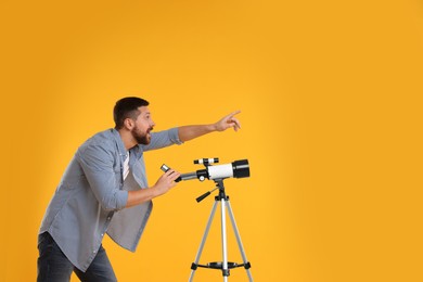 Photo of Excited astronomer with telescope pointing at something on orange background. Space for text