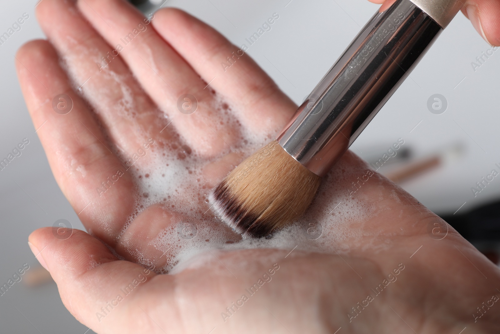 Photo of Woman washing makeup brush with soap, closeup