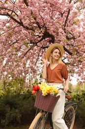 Photo of Beautiful young woman with bicycle and flowers in park on pleasant spring day