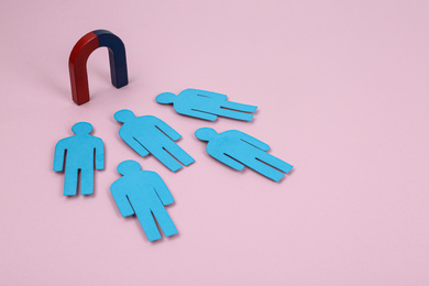 Photo of Magnet attracting paper people on pink background