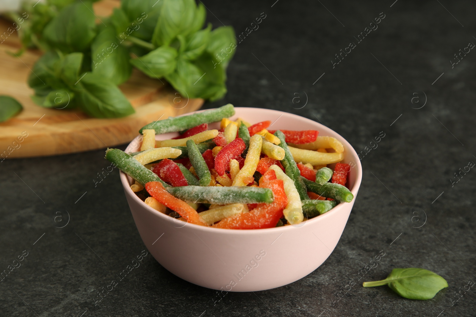 Photo of Bowl of different frozen vegetables on grey table, closeup