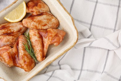 Photo of Raw marinated chicken wings, rosemary and lemon in baking dish on cloth, top view. Space for text