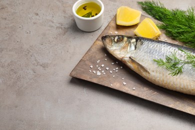Photo of Board with delicious salted herring, dill, lemon and olive oil on grey table, space for text