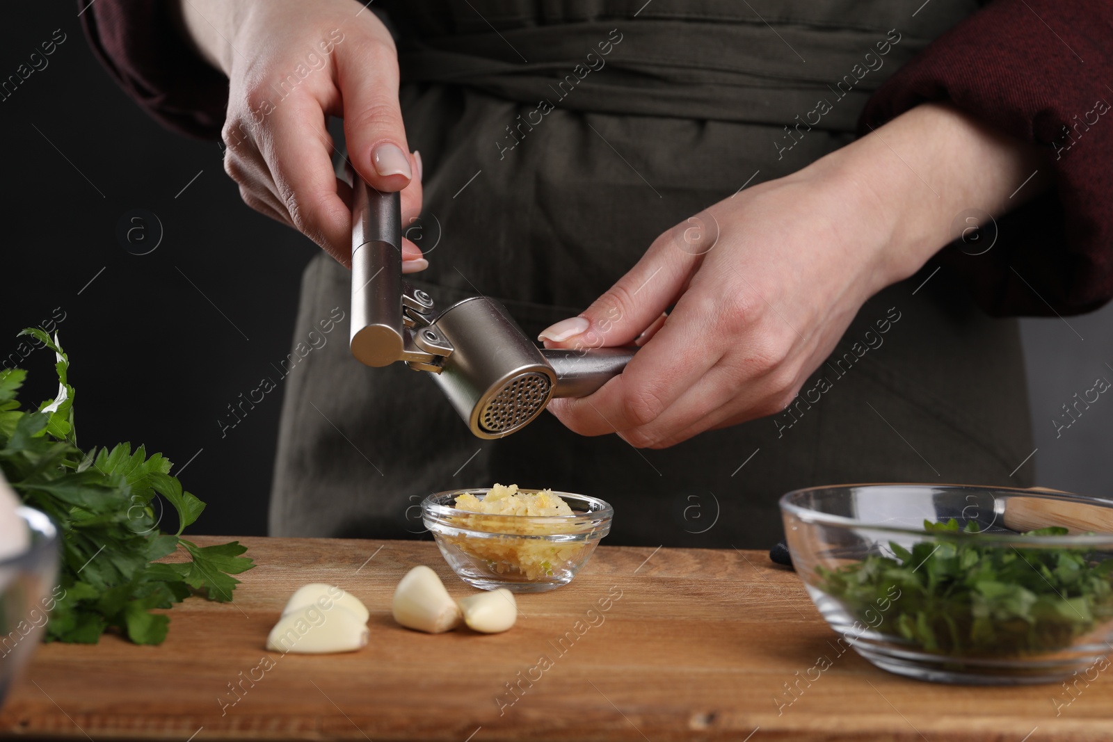 Photo of Woman squeezing garlic with press at wooden table, closeup