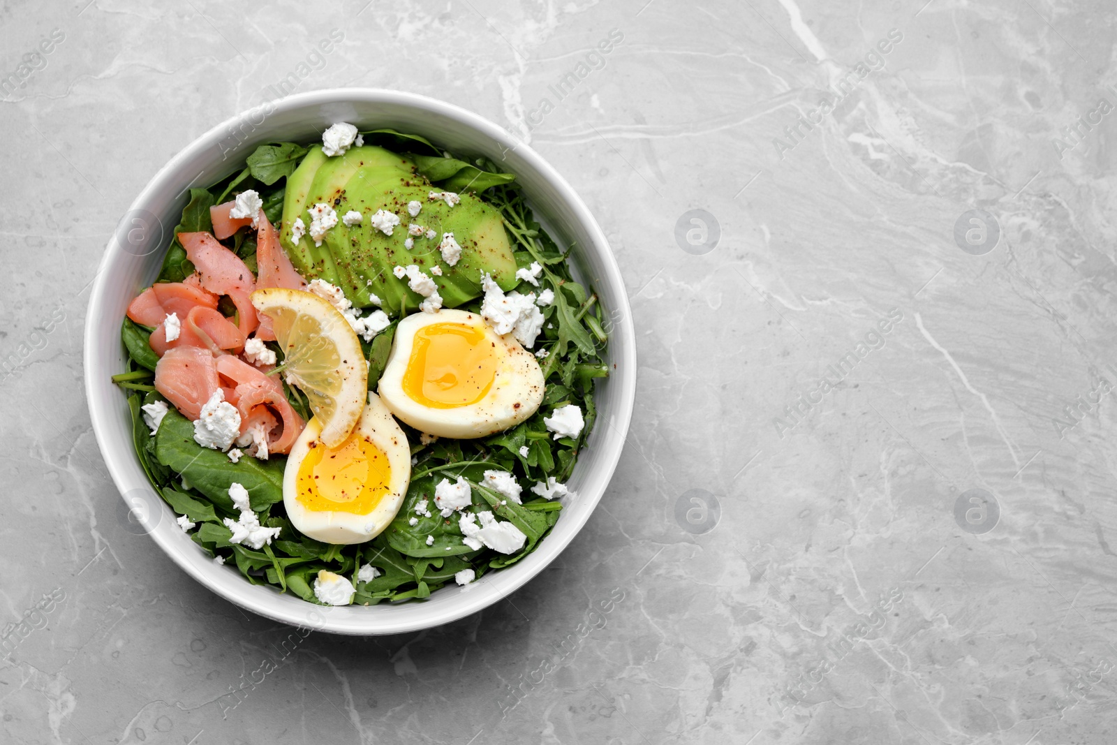 Photo of Delicious salad with boiled egg, salmon and cheese in bowl on light grey marble table, top view. Space for text