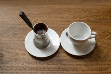 Jezve with fresh coffee and empty cup on wooden table