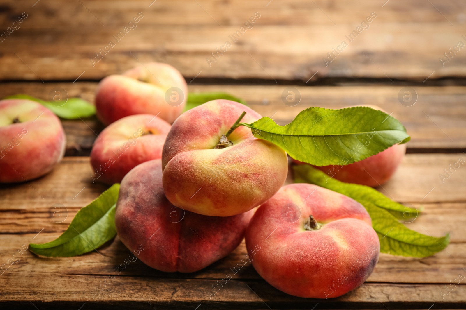 Photo of Fresh ripe donut peaches with leaves on wooden table, closeup