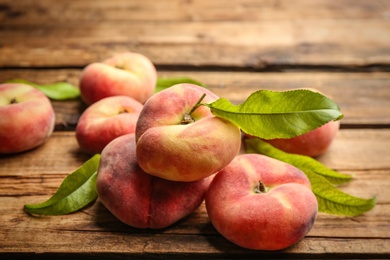 Photo of Fresh ripe donut peaches with leaves on wooden table, closeup