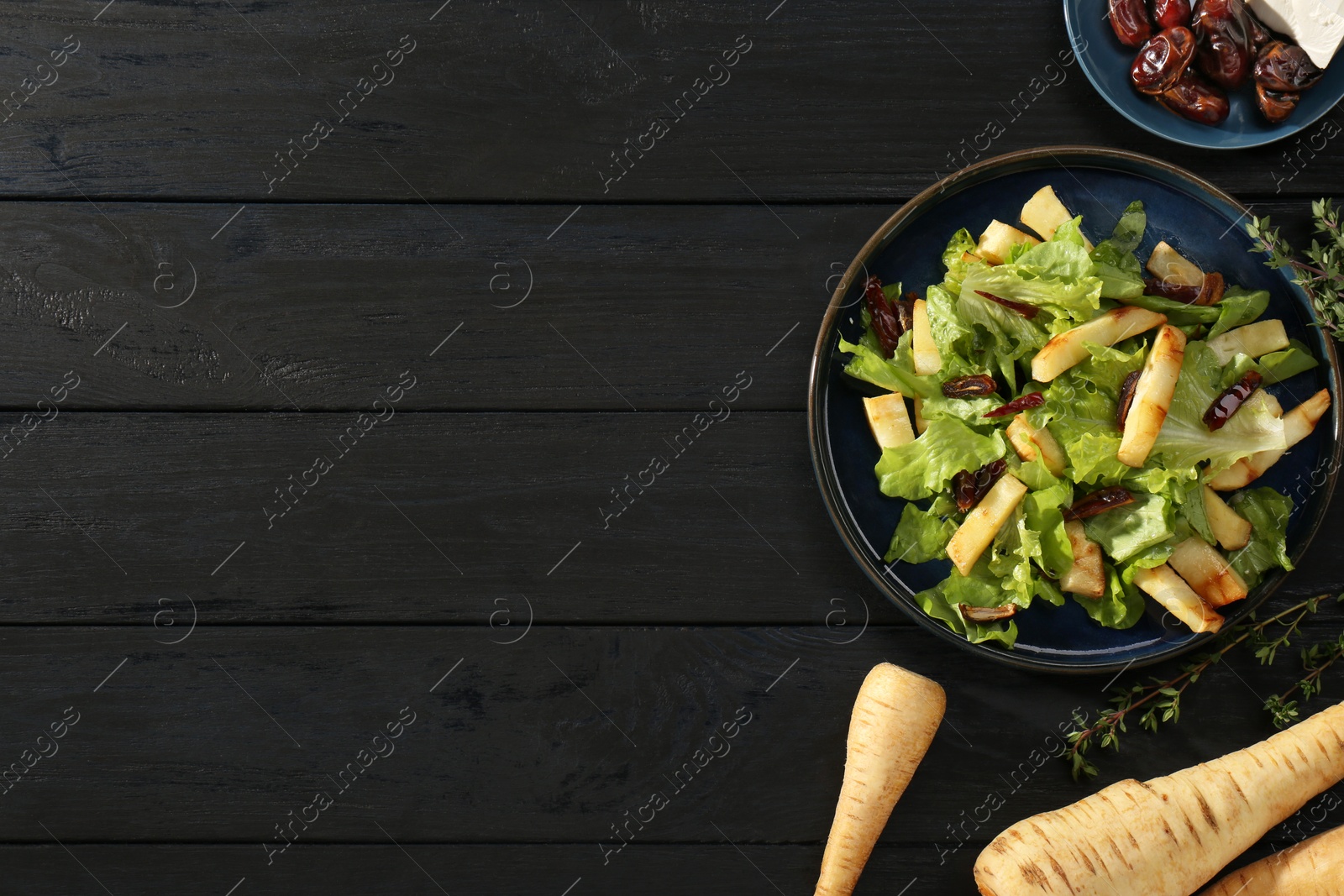 Photo of Delicious parsnip with lettuce and dates on black wooden table, flat lay. Space for text